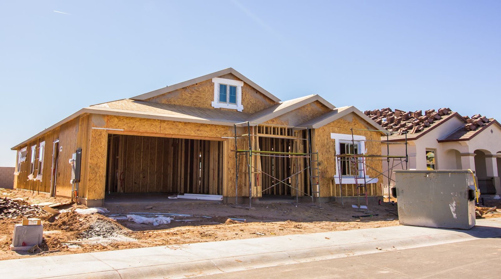 Oak Grove Estates home mid-construction: framed and sheathed, scaffolding up, roof tile staged on the neighboring build